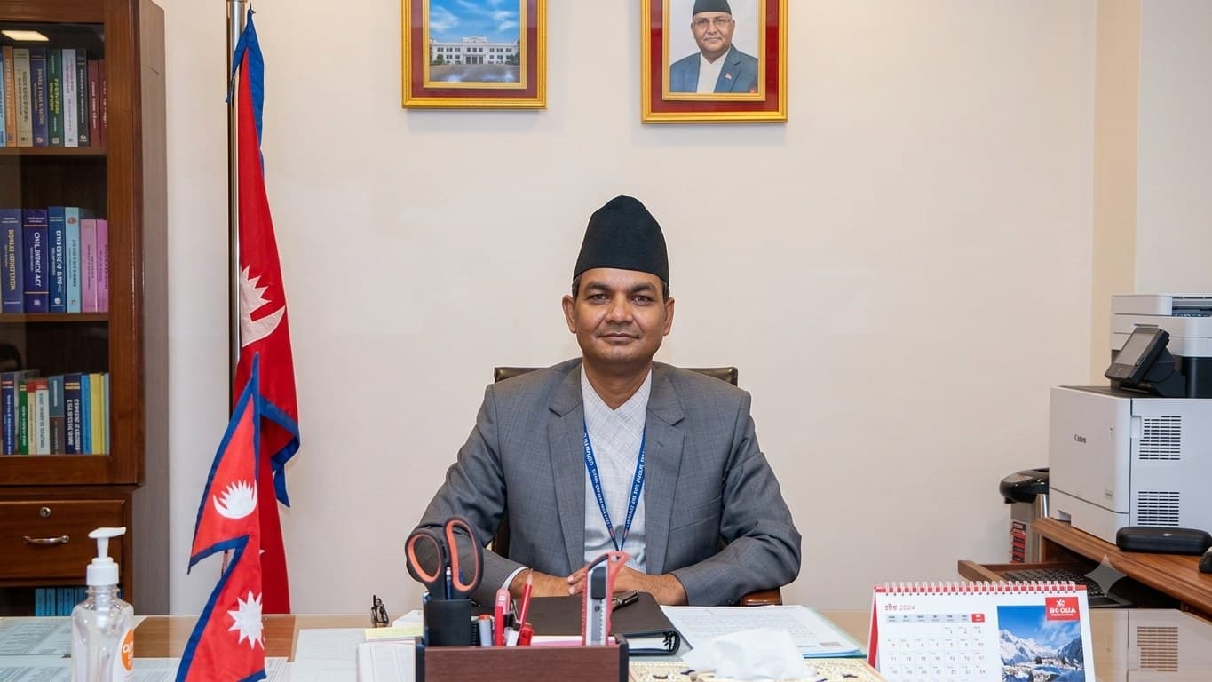 Dr. Krishna Hari Pushkar at his desk, flanked by the flags of Nepal